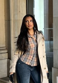 Cappotto trench beige chiaro, camicia a quadri con accenti rossi e blu navy, jeans aderenti e guanti neri. Texture lisce, elementi di design classici.