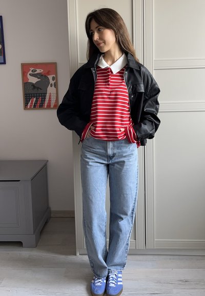 Camisa de polo a rayas rojas y blancas debajo de una chaqueta de cuero negra, combinada con jeans de color azul claro y zapatillas azules con rayas blancas.