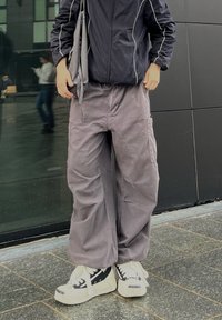 Pantalons cargo gris amples en tissu doux, avec des poches latérales, associés à des baskets chunky blanches et noires, et une veste à zip sombre.