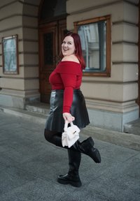 Κόκκινος πουλόβερ σε στυλ off-the-shoulder, μαύρη φούστα από τεχνητό δέρμα, μαύρες γόβες μέχρι το γόνατο και λευκή τσάντα με χρυσές λεπτομέρειες. Λείες υφές και κομψός σχεδιασμός.