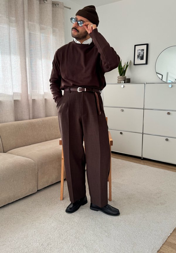 Hnedý pletený sveter, hnedé vysoký pás na mieru so záhybmi, čierny opasok, čierne topánky a hnedá čiapka v rovnakom odtieni. Svetlé vnútorné osvetlenie.