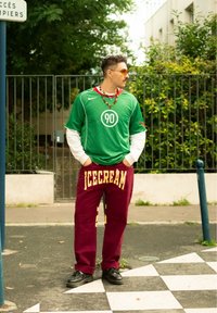 Maillot Nike vert avec des manches blanches et un logo "90", associé à un pantalon de survêtement bordeaux avec "ICECREAM" en jaune. Chaussures et accessoires noirs.
