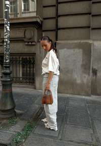 Hétköznapi öltözet, amely egy oversized fehér pólóból, világoskék farmerból és egy kicsi barna táskábból áll. Fehér szandálokkal és napszemüveggel viselve.