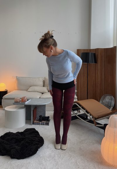 Medias de color burdeos con un diseño de diamantes, combinadas con un suéter ajustado de color azul claro y pantalones cortos negros, en un fondo interior acogedor.