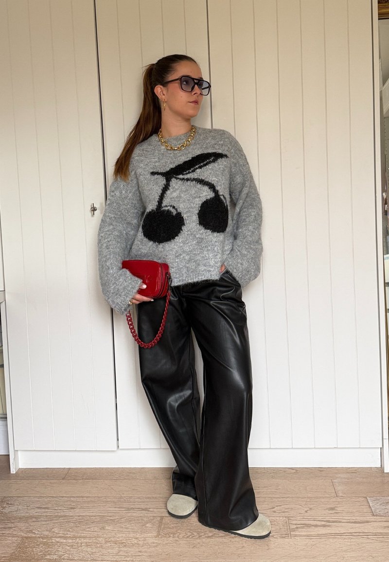 Gray sweater with black cherry design, black faux leather wide-leg pants, red handbag with chain, and beige slippers on a wooden floor.