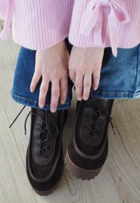 Hnedé šnurovacie topánky s kombináciou hladkých a semišových textúr, so silnou podrážkou a vlnitým zdobením pozdĺž okrajov.