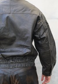 Svart skinnjakke med strukturert finish, elastisk midje og rynkede mansjetter. Har et strukturert design med minimale sømdetaljer.