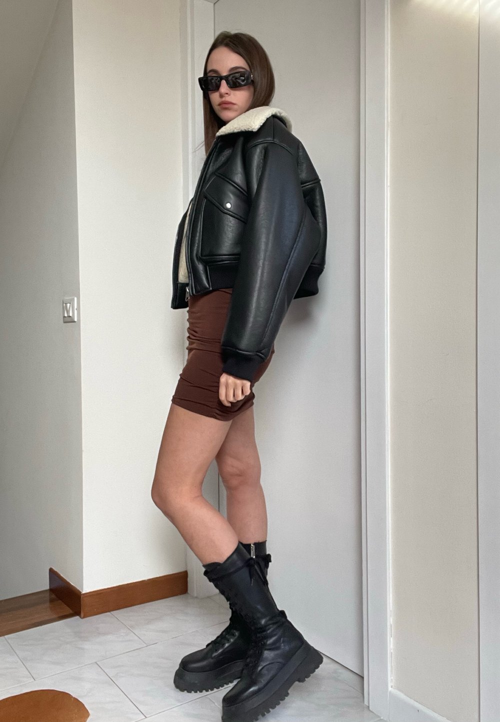 Svart läderkort jacka med en beige faux shearling-krage, ihopparad med en brun rynkad minikjol och svarta kängor.