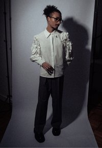 Λευκό βαμβακερό πουκάμισο με ριγέ μανίκια, σε συνδυασμό με σκούρες γκρι παντελόνες. Το μοντέλο φοράει γυαλιά και στέκεται σε φωτεινό φόντο με απαλό φωτισμό.