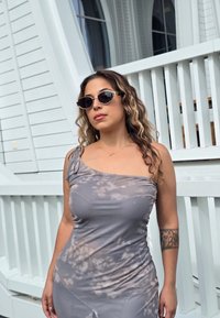 Sivél, batikovaný šaty s jedným ramenom, s priliehavým živôtikom a bočným rozparkom. Nosí sa s čiernymi slnečnými okuliarmi so striebornými ozdobami.