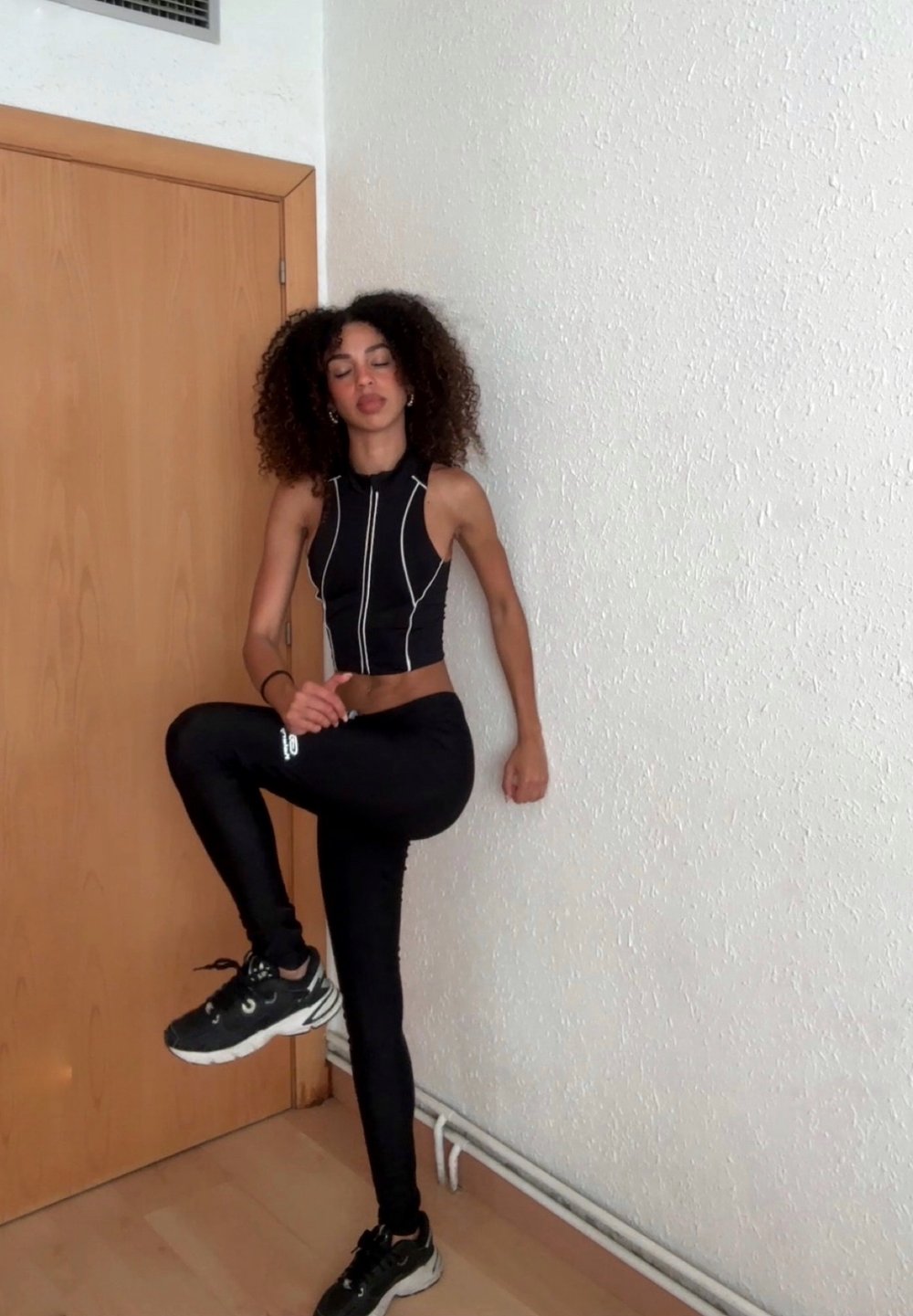 Conjunto desportivo com um top cropped sem mangas preto com costuras brancas, leggings pretas e ténis pretos com detalhes brancos.