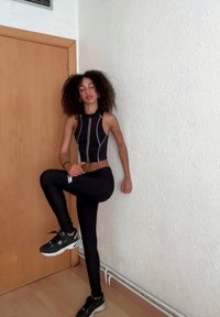Conjunto desportivo com um top cropped sem mangas preto com costuras brancas, leggings pretas e ténis pretos com detalhes brancos.