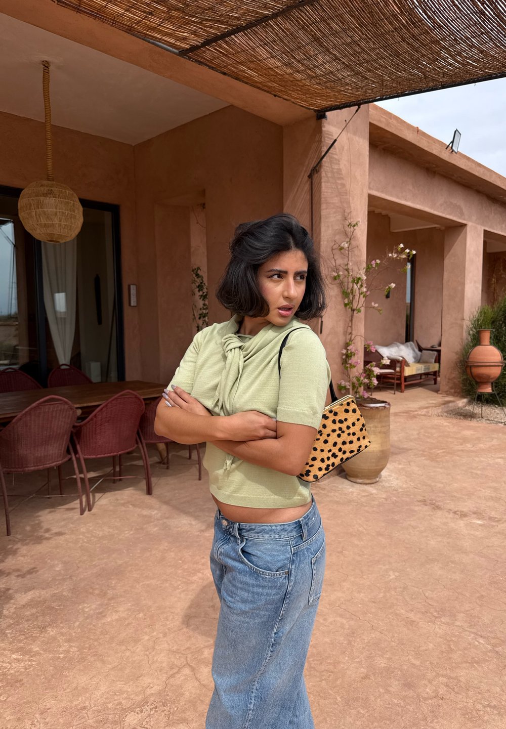 Hellgrüner, kurz geschnittener Pullover mit einem Knoten-Detail, kombiniert mit hoch taillierten blauen Denim-Jeans und einer kleinen Tasche mit Tierprint.