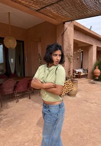 Hellgrüner, kurz geschnittener Pullover mit einem Knoten-Detail, kombiniert mit hoch taillierten blauen Denim-Jeans und einer kleinen Tasche mit Tierprint.