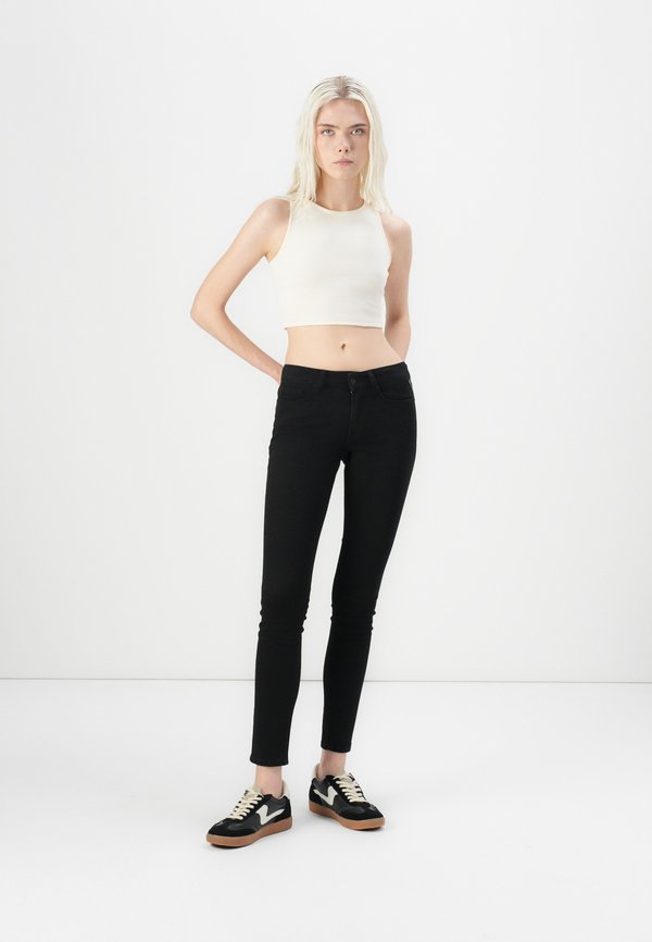Black skinny jeans featuring front pockets and a zip closure, styled with a fitted white ribbed crop top and black sneakers with a gum sole.