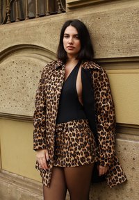Leopardí vzorovaný kabát cez čierny body a zodpovedajúce šortky. Má hladkú tkaninu, golier a pás s opaskom s vysokým strihom po stehno.