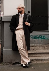 Μαύρο παλτό, μπεζ πλεκτό πουλόβερ, μπεζ παντελόνι, μαύρη ζώνη, στρογγυλά γυαλιά και ανοιχτό μπεζ σκουφί. Μαύρα παπούτσια με λευκές λεπτομέρειες.