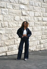 Denim jacket and wide-leg jeans in dark blue, paired with a white crop top. The outfit features a relaxed fit and distinct pockets.