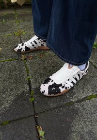 Kylleprinte sko lavet af læder, med hvide accenter og sorte striber. Sålen er beige, med en glat tekstur og sporty design.
