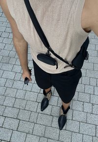 Μπεζ ριγωτό πουλόβερ, μαύρες βερμούδες, μαύρη τσάντα χιαστί και μαύρες μποτάκια με γωνιακή μύτη και ταμπά λεπτομέρειες. Κρατά γυαλιά ηλίου στο αριστερό χέρι.