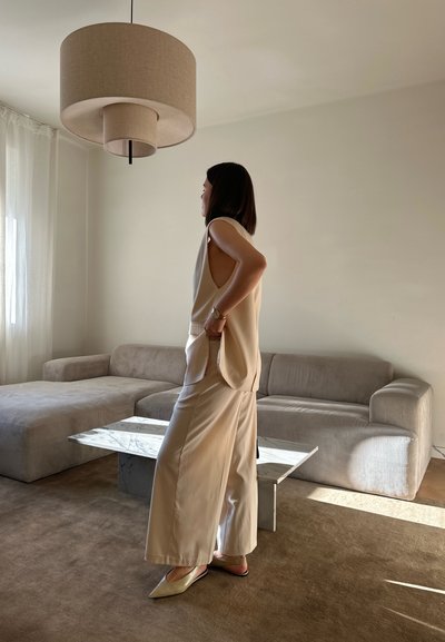 Top sin mangas beige y pantalones de pierna ancha, combinados con zapatos planos de punta. Tejido ligero, diseño minimalista y un ajuste relajado. Mesa de mármol al fondo.