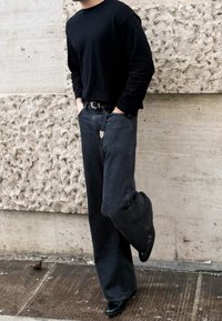 Camicia nera a maniche lunghe abbinata a pantaloni grigi scuri a gamba larga. I pantaloni presentano una finitura testurizzata e una fibbia della cintura in tono argentato.