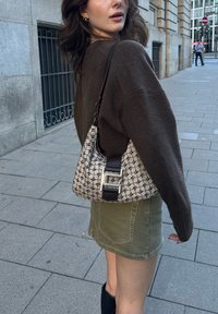 Hobo krepšys, pagamintas iš raštuoto audinio smėlio ir juodos spalvos, su rudomis odinėmis rankenomis ir sidabro detalėmis. Modelis vilki rudą megztinį ir žalią sijoną.