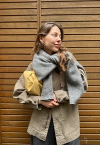 Beige oversized jakke, grå strikket tørklæde, gul læderhåndtaske. Træbaggrund. Casual outfit med strukturerede materialer.