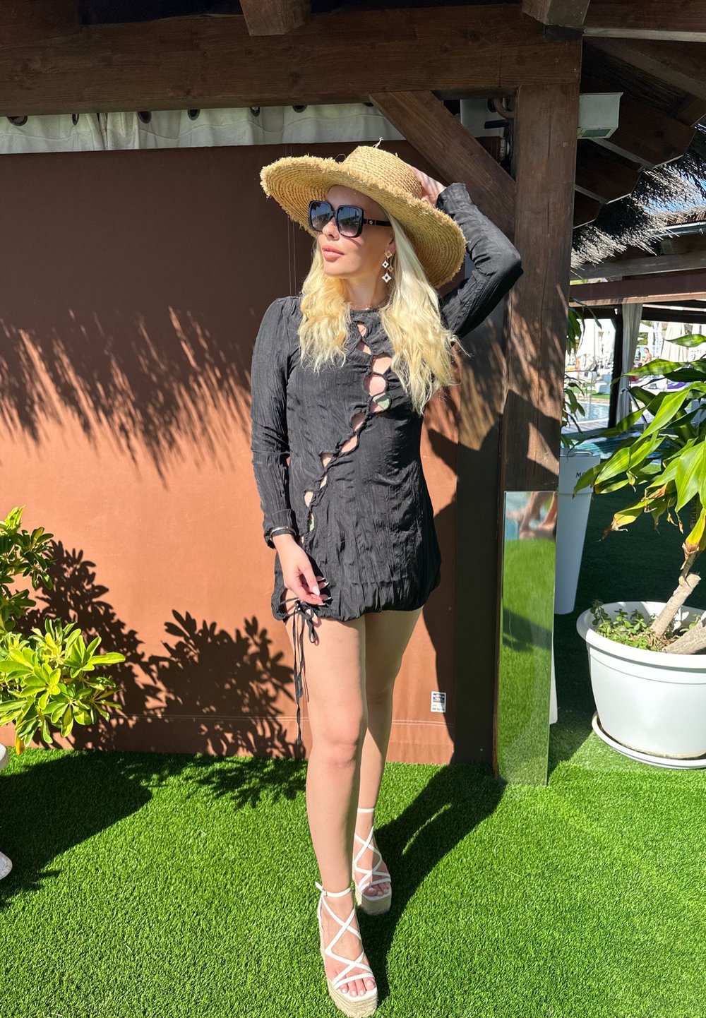 Vestido preto de mangas longas com decote arredondado e detalhes recortados, ajustado na cintura. Acompanhado de um chapéu de palha e sandálias espadrilles brancas.