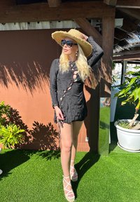 Vestido preto de mangas longas com decote arredondado e detalhes recortados, ajustado na cintura. Acompanhado de um chapéu de palha e sandálias espadrilles brancas.