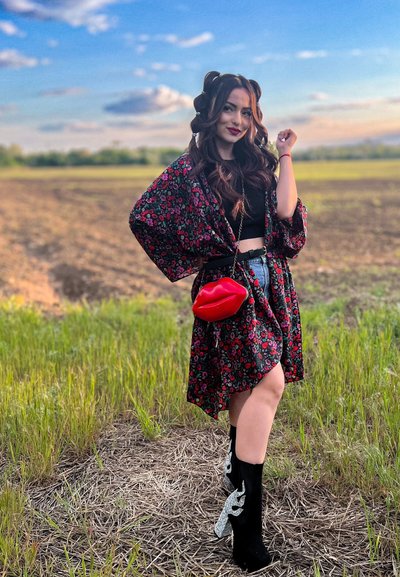 Kimono negro con flores sobre una camiseta corta negra, pantalones cortos de mezclilla y botas negras hasta la rodilla con acentos de llama plateados; bolso en forma de labios rojos.