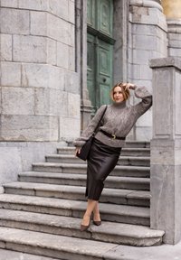 Szary wełniany sweter z golfem, ozdobiony wzorami w warkocze, połączony z czarną skórzaną spódnicą ołówkową. Modelka dobrała czarną torebkę i szpilki.