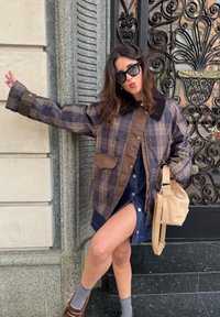 Brūna un raibā jakas ar melnu apkakli, priekšējām kabatām, valkāta virs tumši džinsu kleitas. Smilškrāsas soma un pelēkas zeķes ar brūnām kurpēm.