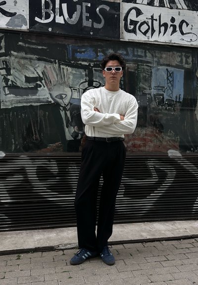 Suéter blanco de manga larga, pantalones de pierna ancha negros y zapatillas azules con tres rayas de color azul claro. Modelo lleva gafas de sol blancas.