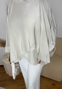 Top supradimensionat, fin, de culoare gri deschis, cu un design fluid și mâneci tip aripă de liliac; asortat cu pantaloni largi albi și un plic țesut.