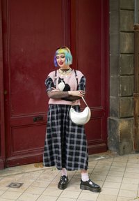 Πλεχτό πουλόβερ με σχέδιο μαύρης γάτας, ροζ χρώμα; μακρύ φούστα σε μαύρο και λευκό καρό; ασημί τσάντα; μαύρα παπούτσια πλατφόρμας; παστέλ μαλλιά.