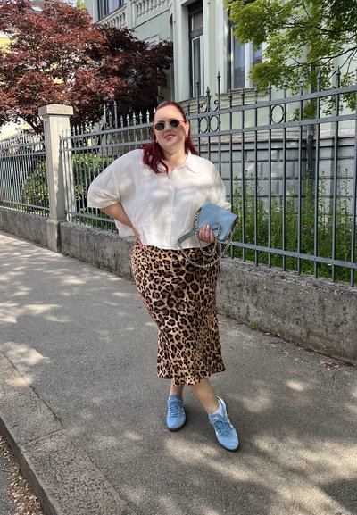 Blusa de lino clara, falda midi con estampado de leopardo, zapatillas deportivas azul claro y un bolso azul con cadena. Paseando por una acera soleada.