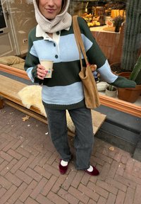 Striktrøje i grønne og lyseblå striber, med en hvid krave og tre knapper. Parret med mørke jeans og burgunder sko. Holder en kaffekop.