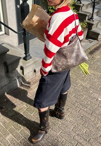 Suéter às riscas vermelhas e brancas, bolsa metálica cinza, calções pretos e botas altas pretas. Segurando um saco de papel castanho com talos verdes.