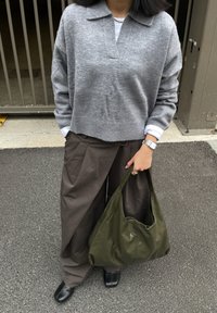 Harmaa villapaita, jossa on kaulus, väljässä istuvissa ruskeissa housuissa ja sileä vihreä laukku. Mustat kengät täydentävät asun kellon kanssa.