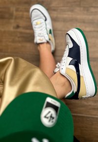 Sneaker Nike Air Force 1 con tomaia in pelle bianca, dettagli in navy e beige, suola verde e particolari in gomma texturizzata.