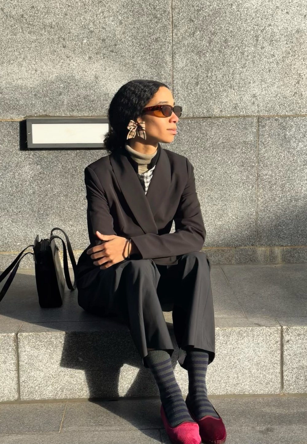 Melnā pielāgotā bleizera virs uzrauta krekla ar rūtiņām, saskaņota ar tumšām biksēm, rozā apaviem un svītrainām zeķēm. Aksesuārs: liels loku auskaru.