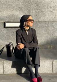 Melnā pielāgotā bleizera virs uzrauta krekla ar rūtiņām, saskaņota ar tumšām biksēm, rozā apaviem un svītrainām zeķēm. Aksesuārs: liels loku auskaru.