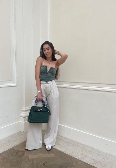 Top verde ajustado sin tirantes con un profundo corte en V, pantalones anchos blancos, bolso verde con una bufanda estampada y zapatos grises sin tacón.
