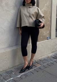 Khaki krótka kurtka z szerokimi rękawami, zestawiona z czarnymi legginsami i czarnymi szpiczastymi szpilkami. Dodatki obejmują teksturowany czarny kopertówka.