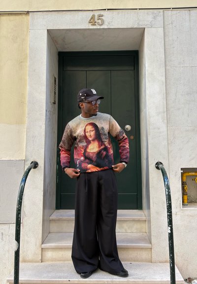 Suéter con estampado de Mona Lisa, con colores vibrantes; combinado con pantalones anchos negros. El fondo incluye una puerta verde oscuro y escalones.
