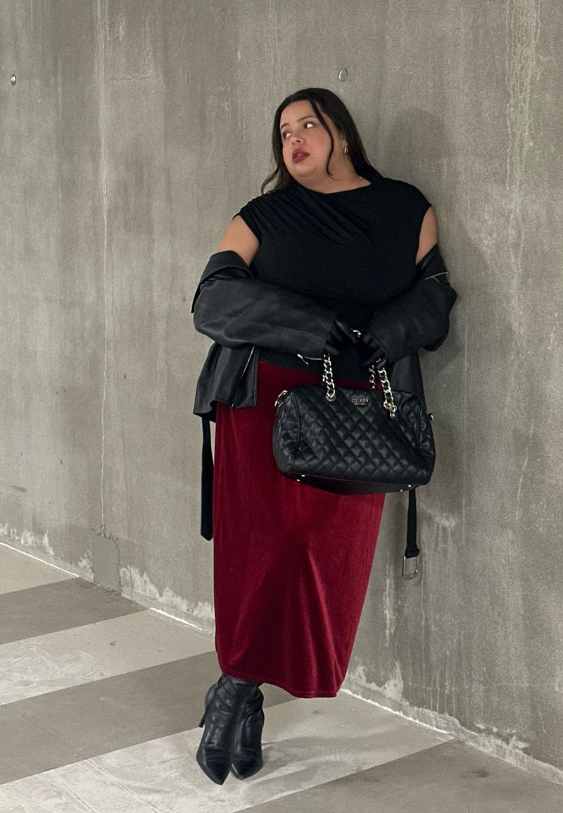 Svart ermeløs topp, rødt fløyelsmaksiskjørt, oversized svart skinnjakke, quiltet svart håndveske og spisse svarte ankelstøvler.