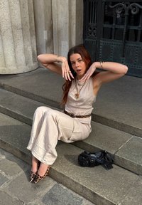 Combinaison beige avec une finition texturée et des jambes larges, ceinture à imprimé léopard, sac à main noir et escarpins à bouts pointus à imprimé léopard. Accents de bijoux en or.