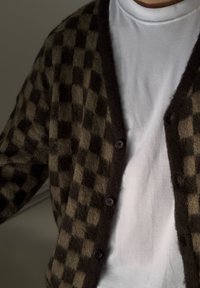 Cárdigan a cuadros marrón y beige hecho de un material suave, con un profundo escote en V, seis botones y llevado sobre una camiseta blanca.