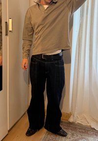 Polo à manches longues gris clair, jean large bleu foncé, ceinture noire et chaussures noires. Couleurs unies, design minimaliste, coupe décontractée.